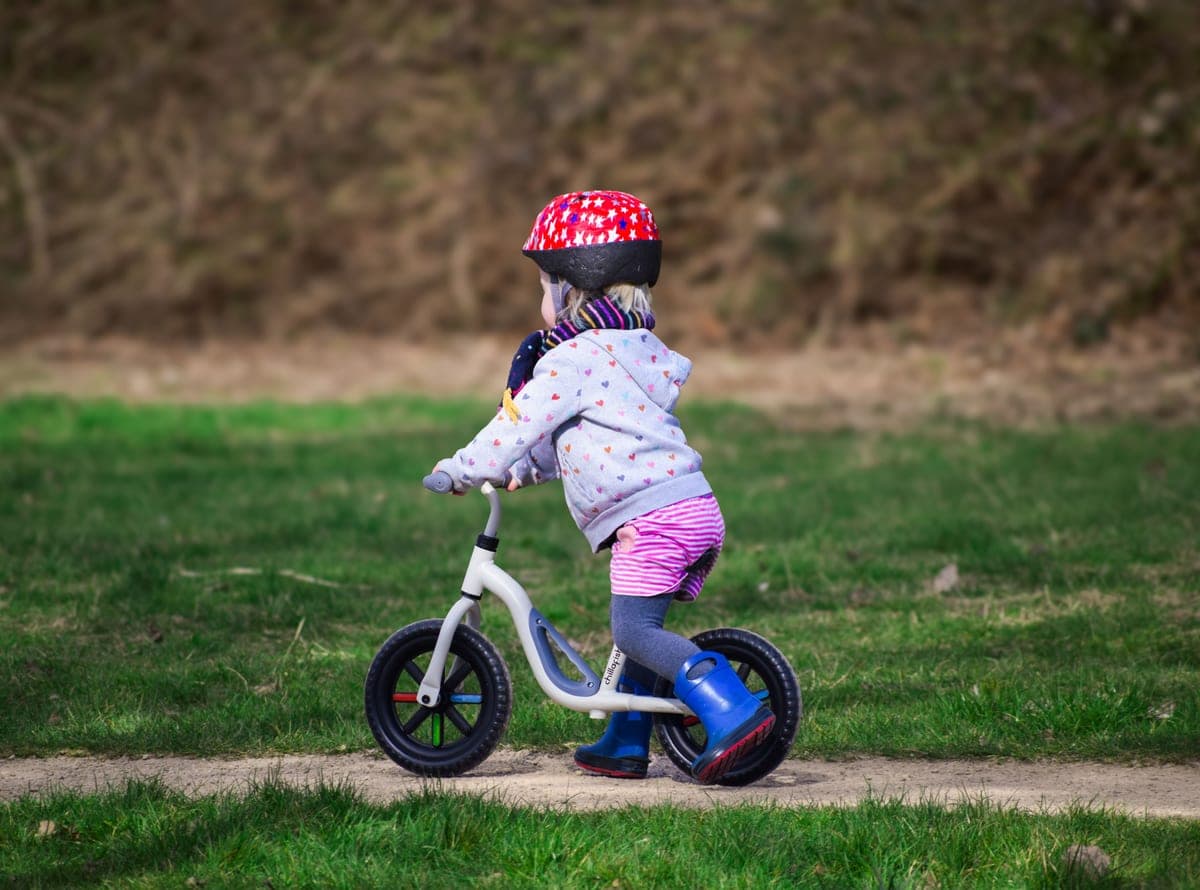 Toddler in a helmet riding a balance bike across grass