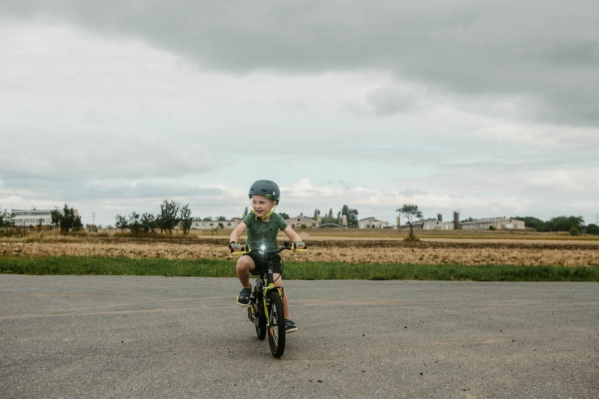 Child in a helmet riding a first pedal bike on an open road