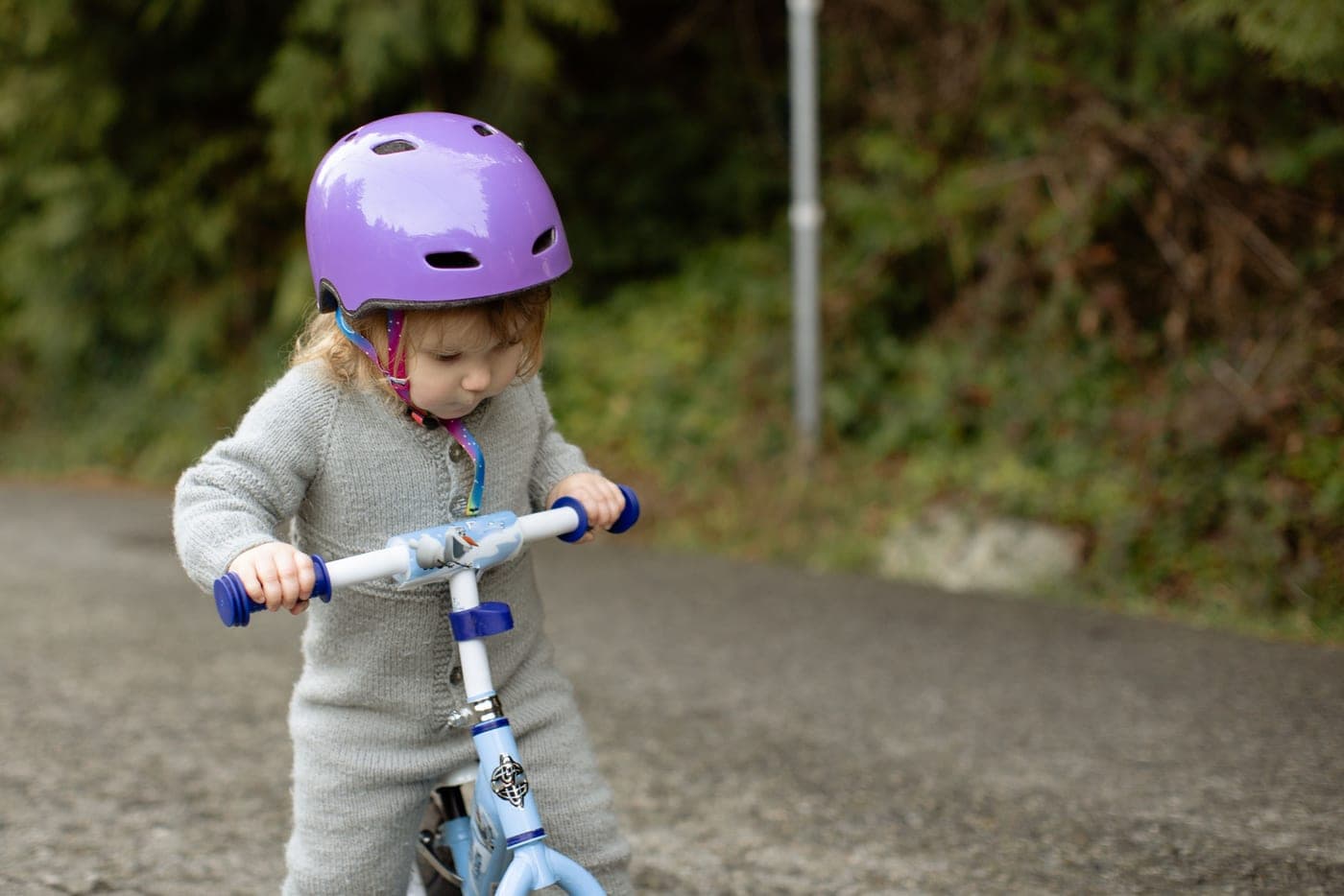 Toddler in a purple helmet riding a blue balance bike on a path